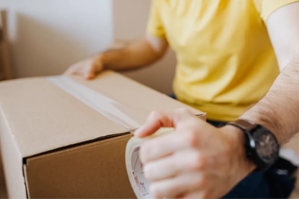 Une personne fermant un carton avec du scotch